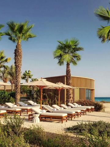 Strand mit Liegen und Palmen neben einem Gebäude am Meer
