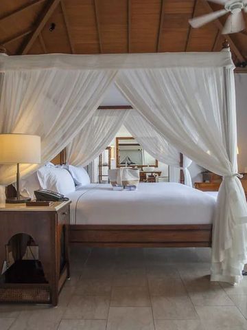 Zimmer mit Himmelbett unter Holzdach und hellen Vorhängen.