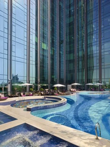 Großer Pool auf einer Hotelterrasse umgeben von hohen Glasfassaden