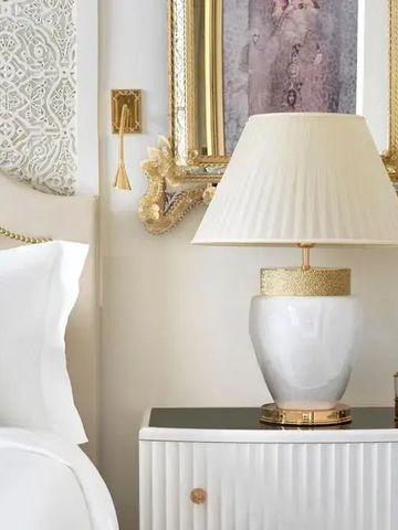 Nachttisch mit edler Lampe und goldgerahmtem Bild neben einem Bett.