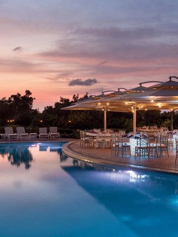 Beleuchteter Poolbereich bei Sonnenuntergang mit Tischen und Stühlen neben dem Wasser.