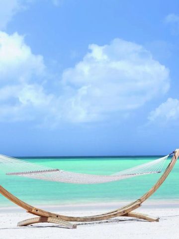 Hängematte am weißen Sandstrand mit türkisfarbenem Meer im Hintergrund.