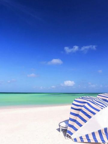 Strand mit gestreiften Sonnenschirmen und Liegestühlen am kristallklaren Wasser.