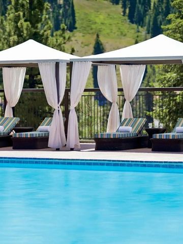 Pool mit weißen Cabanas und bequemen Liegen vor grüner Waldkulisse