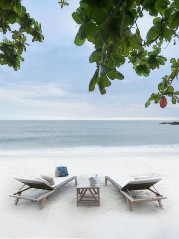 Weißer Sandstrand mit zwei Sonnenliegen unter grünem Blätterdach