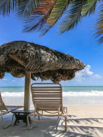 Zwei Strandliegen unter einem Strohdach mit Blick aufs Meer