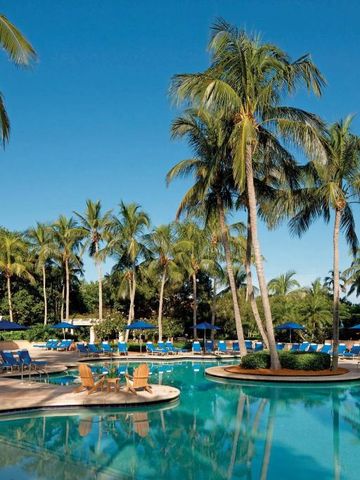 Tropischer Poolbereich mit Palmen und Liegen unter blauem Himmel