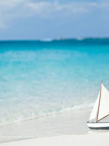 Miniatursegelboot am weißen Sandstrand mit türkisfarbenem Meer im Hintergrund