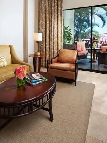 Sitzecke in einem Hotelzimmer mit Zugang zu einer Terrasse und Blick auf Palmen.