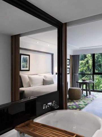 Schlafzimmer mit Blick ins Grüne und separater Badewanne im Vordergrund.