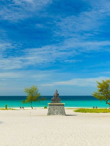 Strand mit einer Buddha-Statue und türkisblauem Meer im Hintergrund bei schönem Wetter