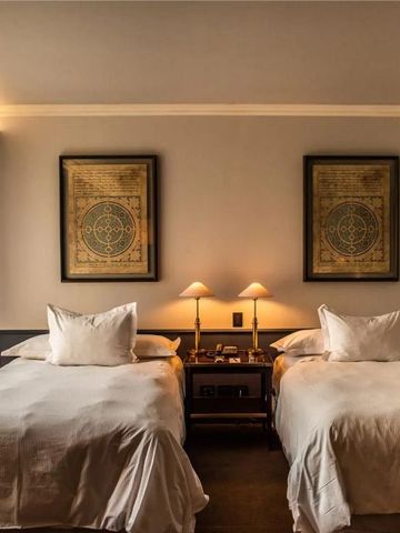 Doppelzimmer mit zwei Betten und dekorativen Kunstwerken an den Wänden.