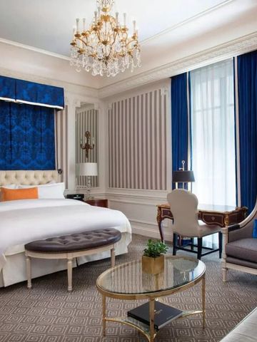 Luxuriös dekoriertes Gästezimmer im St. Regis New York mit blauen Vorhängen und klassischen Möbeln.