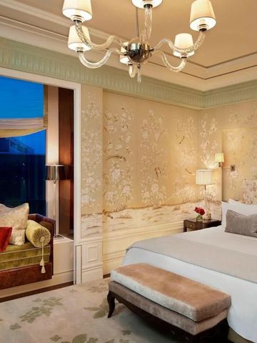 Luxuriöses Hotelzimmer mit Bett, Leuchter und Tagesbett vor einem großen Fenster