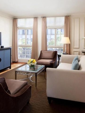 Helles Wohnzimmer einer Hotelsuite mit modernem Sofa, Sessel und großem Fenster.