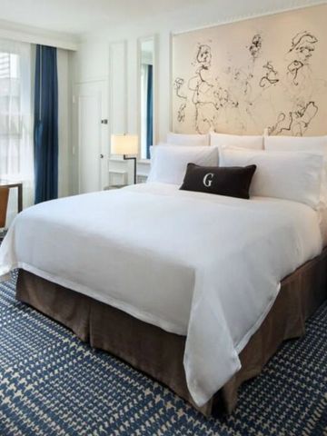 Elegantes Hotelzimmer mit großem Bett, blauen Akzenten und Kunst an der Wand.