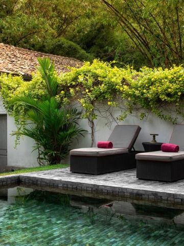 Zwei Sonnenliegen am Rand eines kleinen Pools inmitten von Pflanzen