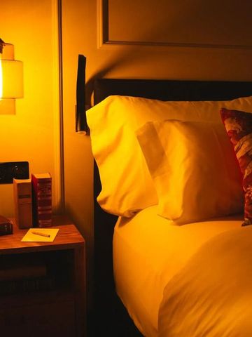 Gemütliches Bett mit stilvoller Beleuchtung und dekorativem Kissen