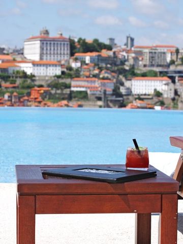 Holztisch mit Drink vor einem Infinity Pool mit Stadthintergrund