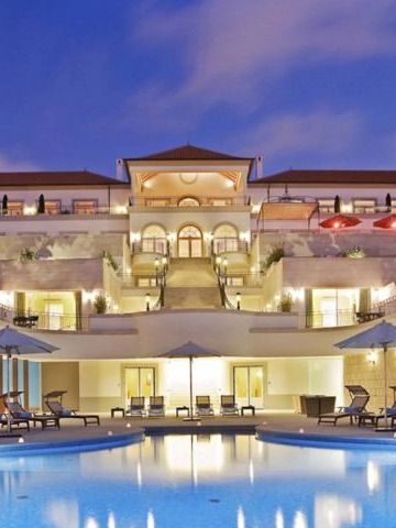 Beleuchtete Hotelanlage bei Nacht mit Pool im Vordergrund und Liegestühlen.