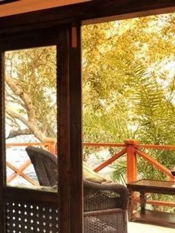 Blick von einer Terrasse mit Sesseln auf den Fluss und umgebende Bäume