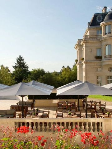 Sonnenterrasse mit Sonnenschirmen vor der eleganten Fassade des Hotels in grüner Umgebung.