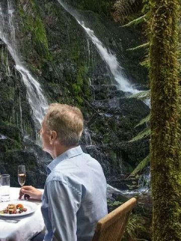 Paar genießt ein romantisches Abendessen im Freien neben einem rauschenden Wasserfall