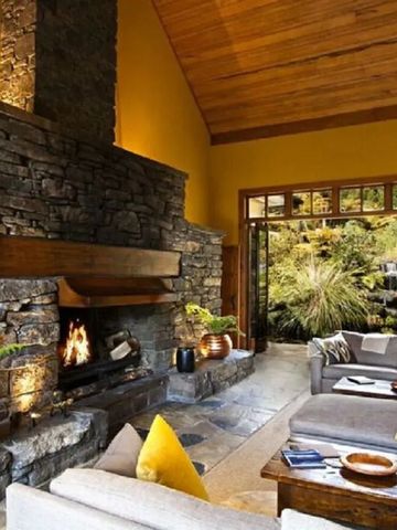 Wohnraum mit offenem Kamin Natursteinwand und großen Fenstern zum Garten