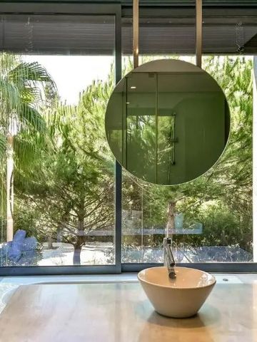 Blick aus einem Badezimmerfenster auf einen grünen Garten mit Palmen.