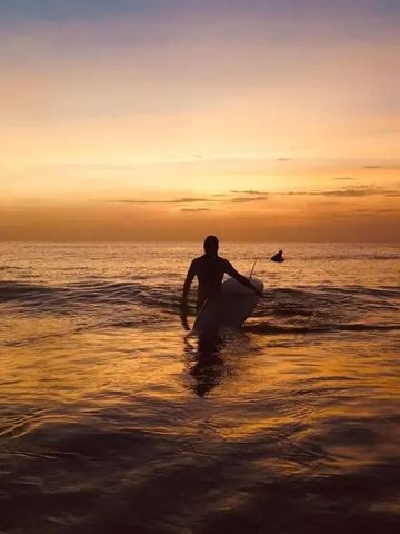 Person mit Surfbrett im Meer bei Sonnenuntergang