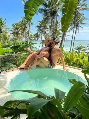 Paar im Infinity-Pool vor tropischer Kulisse mit Meerblick