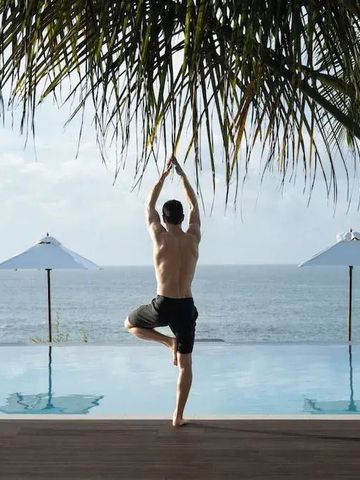 Person praktiziert Yoga am Infinity-Pool mit Meerblick