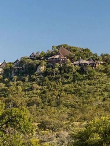 Ulusaba Rock Lodge auf einem Hügel inmitten üppiger Vegetation bei klarem Himmel