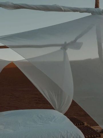 Bett in Wüstencamp mit transparentem Baldachin und Sanddünen