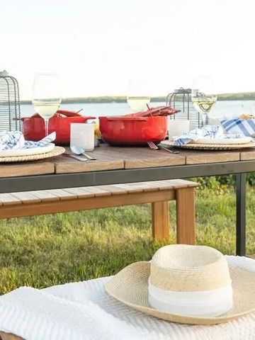 Eleganter Picknicktisch im Freien mit Geschirr und Hüten in Seenähe.