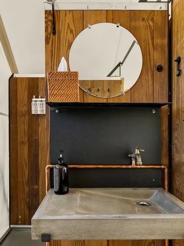 Stilvolles Waschbecken in einem Zelt mit Holzverkleidung und rundem Spiegel
