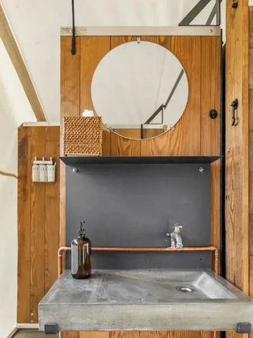 Rustikales Badezimmer in einem Zelt mit Holzverkleidung und rundem Spiegel