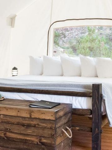 Zelt mit großem Bett und Holzmöbeln in einer naturnahen Umgebung falls es ein Hotelzimmer ist.