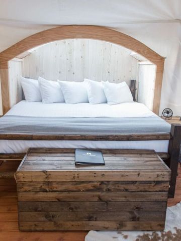 Gemütliches Zeltzimmer mit großem Bett, Holzmöbeln und Laternen.