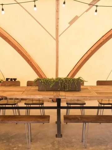 Großer Holztisch mit Hockern in rustikaler Zeltatmosphäre mit Pflanzenarrangement