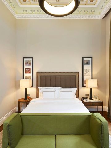 Hotelzimmer mit Kingsize-Bett, grüner Couch und stilvollen Lampen.