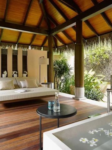 Offene Lounge mit Tagesbett und botanischer Dekoration unter Holzdecke.