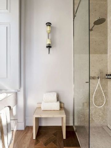 Elegantes Badezimmer mit einer Glasdusche und hellem Holzstuhl mit Handtüchern.