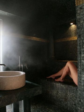 Dampfbad mit schwarzen Mosaikfliesen und steinerner Waschschale
