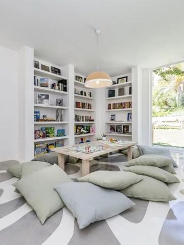 Heller Raum mit Bücherregalen und Sitzkissen auf gemustertem Boden
