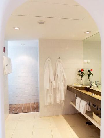 Elegantes Badezimmer mit Bademänteln, frischen Blumen und großzügiger Beleuchtung