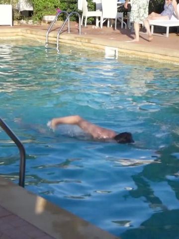 Mann schwimmt im Außenpool des Villa Athena Resort umgeben von Liegestühlen