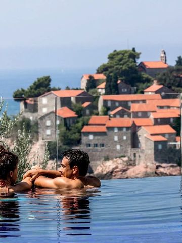 Paar entspannt sich im Infinity-Pool mit Aussicht auf Häuser mit roten Dächern und Meer.