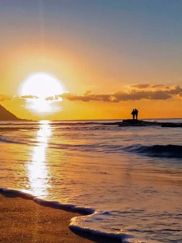Sonnenuntergang an einem Strand mit Klippe und Personen im Wasser
