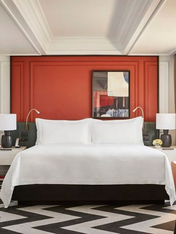 Elegantes Hotelzimmer mit orangefarbener Akzentwand und luxuriösem Doppelbett